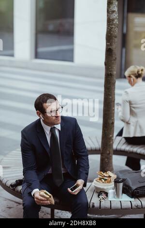 Entrepreneur with smart phone looking away while sitting in city Stock Photo