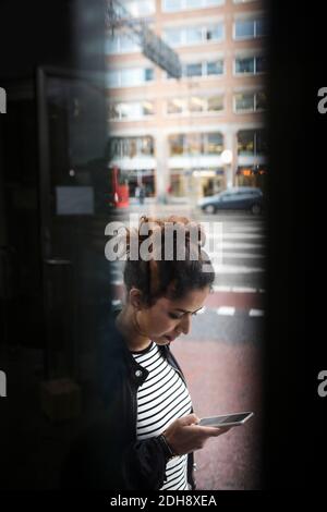 Woman using phone by city street seen through window