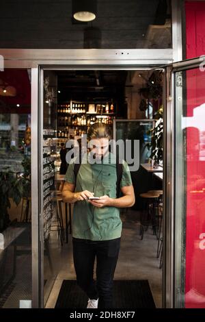 Full length of man using mobile phone while walking at restaurant doorway Stock Photo