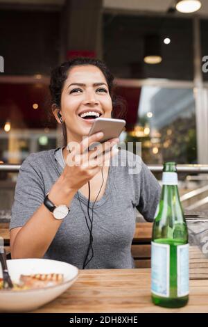 Happy woman using mobile phone while sitting at sidewalk cafe Stock Photo