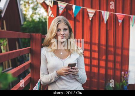 Portrait of teenage girl using mobile phone against house in back yard Stock Photo