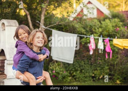 Happy teenage boy giving piggyback ride to friend at back yard Stock Photo