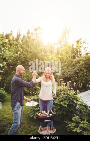 Happy father and daughter giving high-five while cooking vegetables on barbecue grill in back yard Stock Photo