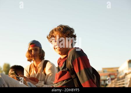 Portrait of smiling male teenager with friends enjoying against clear sky Stock Photo