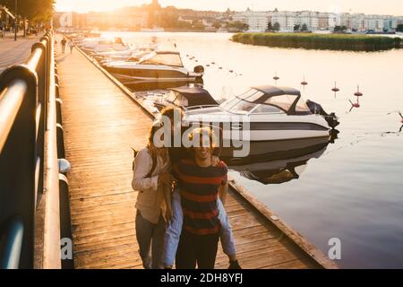Smiling young man giving piggyback ride to male friend at harbor Stock Photo