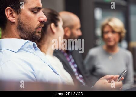 Side view of businessman using mobile phone by colleagues at office yard Stock Photo