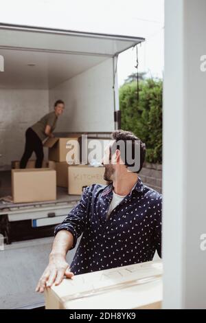 Smiling male looking at female friend while unloading cardboard boxes outside van Stock Photo