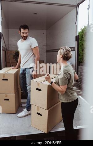 Male and female friends talking while unloading cardboard boxes during relocation Stock Photo