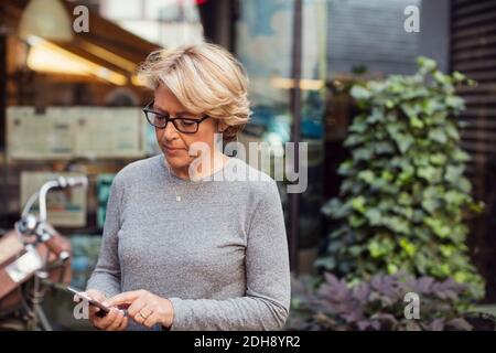 Mature businesswoman using smart phone at sidewalk cafe Stock Photo