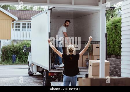 Rear view of female with arms raised cheering while smiling male partner unloading boxes Stock Photo