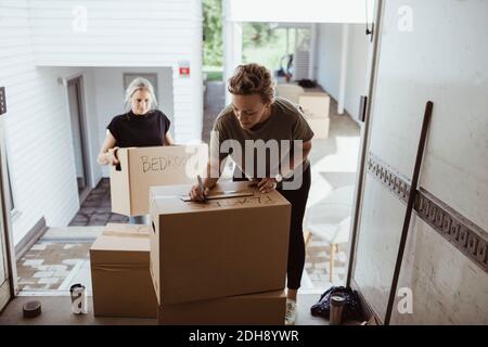 Woman holding box while female writing on cardboard box in moving van Stock Photo