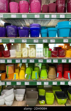 Variety of colorful flower pots are sold at the store. Rows of different pots for indoor plants on shelves in a mall. Vertical view. Stock Photo