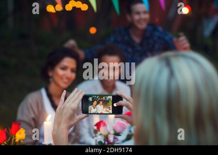 Cropped image of woman photographing happy friends through smart phone at garden party Stock Photo