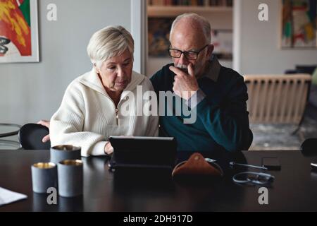 Senior couple using digital tablet while sitting by dining table in living room Stock Photo