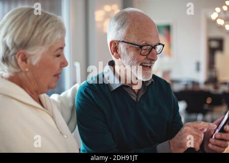 Smiling senior couple using smart phone while sitting in living room Stock Photo