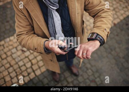 Low section of man using phone while checking the time on footpath Stock Photo
