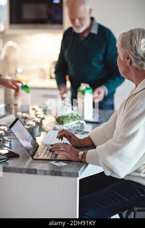 Senior woman using laptop while male partner standing by kitchen island Stock Photo