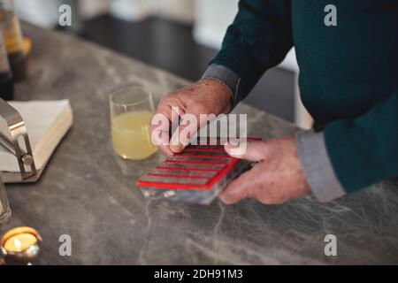 Midsection of senior man taking pills by kitchen island at home Stock Photo