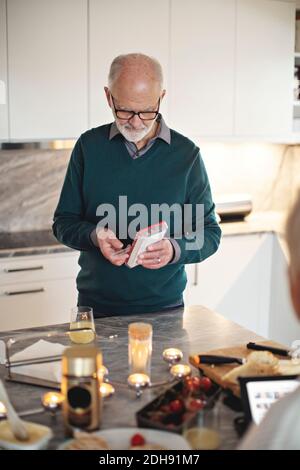 Senior man taking pills while standing by kitchen island at home Stock Photo