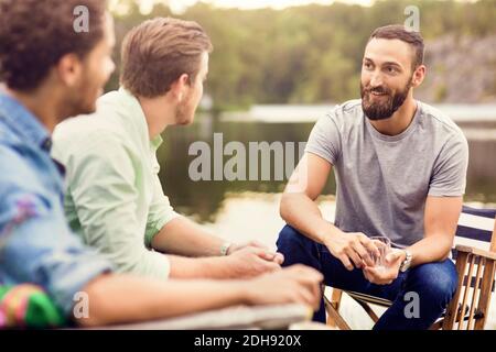 Smiling friends talking while having drink at lakeshore Stock Photo