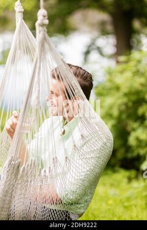 Smiling man having drink while resting in hammock Stock Photo