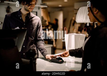 Side view of female customer paying through smart phone at store Stock Photo