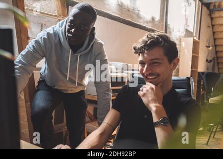 Smiling computer programmer by coworker working on coding at workplace Stock Photo
