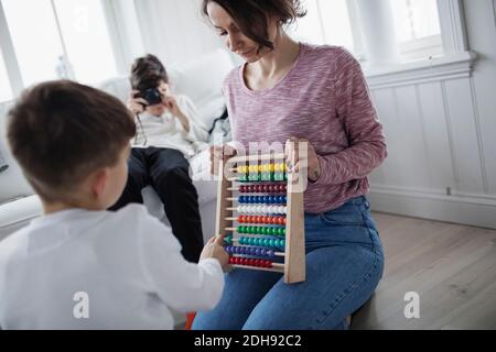 Mother holding abacus while son playing at home Stock Photo