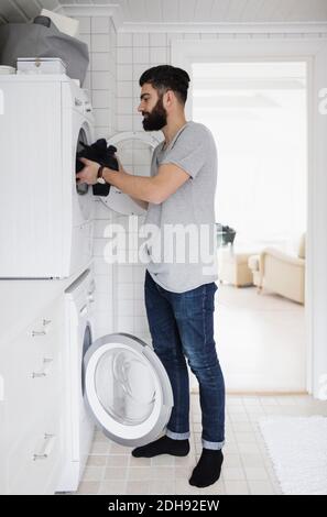 Side view of man loading clothes in washing machine at home Stock Photo