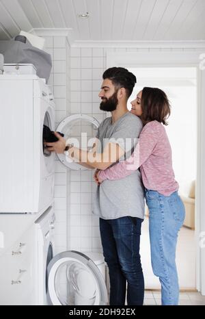 Woman embracing man while loading clothes in washing machine at home Stock Photo