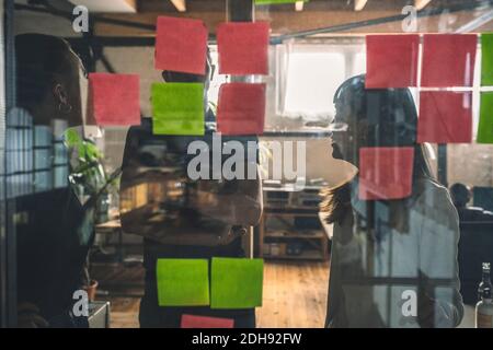Male an female coworkers discussing over sticky notes seen through glass door Stock Photo