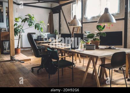Empty laptop and computer arranged on table by chairs at workplace Stock Photo