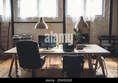 Laptop and computer arranged on table by chairs at workplace Stock Photo