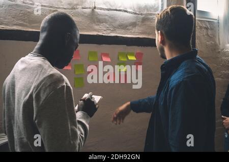 Male coworkers sticking notes on wall at workplace Stock Photo