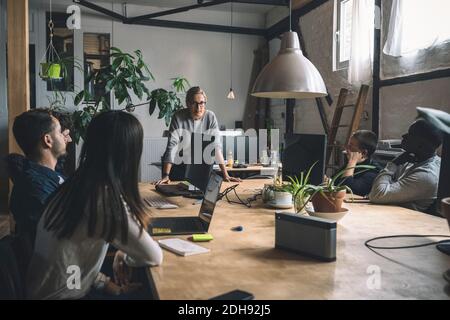Businesswoman discussing with colleagues while standing by table at workplace Stock Photo