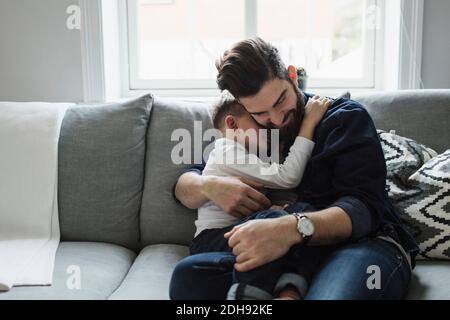 Father embracing son while sitting on sofa at home Stock Photo