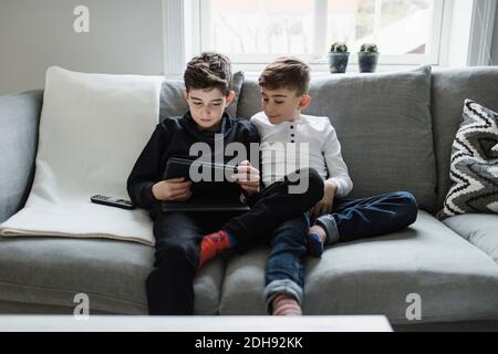 Boy looking at brother using digital tablet while sitting on sofa in living room Stock Photo