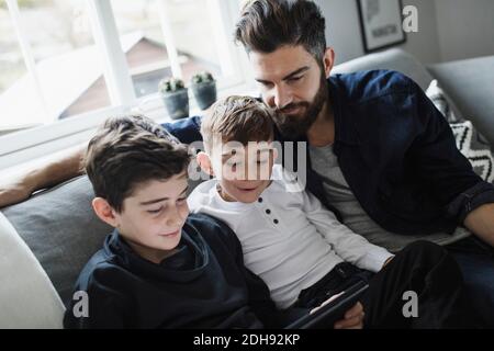 Tilt shot of father and son looking at boy using digital tablet in living room Stock Photo