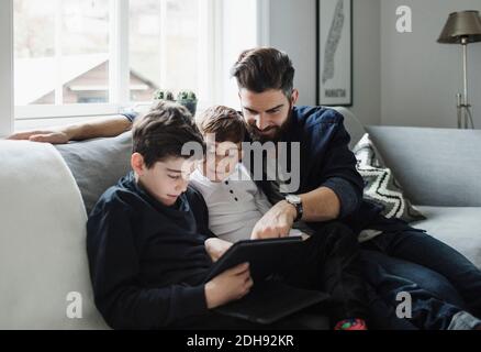 Father and sons using tablet while sitting on sofa at home Stock Photo