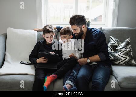 Father and son looking at boy using digital tablet while sitting on sofa Stock Photo