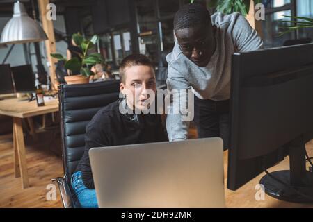 Computer programmer by female coworker using laptop at workplace Stock Photo