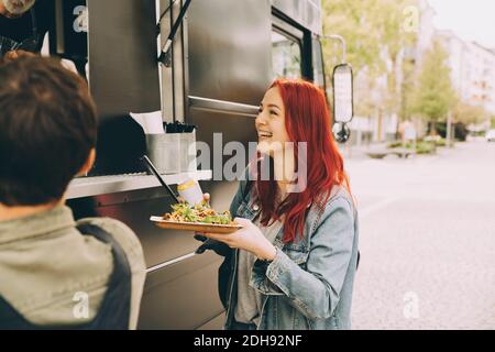 Smiling female customer talking to owner while standing with food plate on street Stock Photo