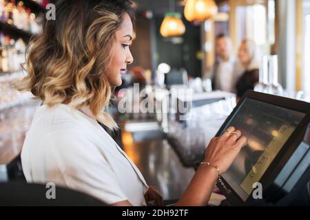 Side view of female owner using cash register at restaurant Stock Photo