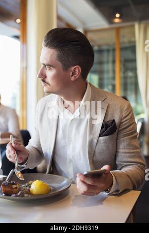 Businessman using mobile phone while looking away at restaurant Stock Photo