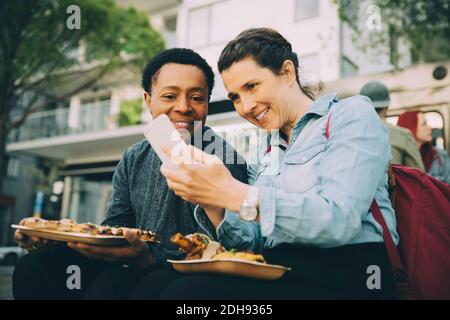 Smiling woman taking selfie with man while eating meal in city Stock Photo