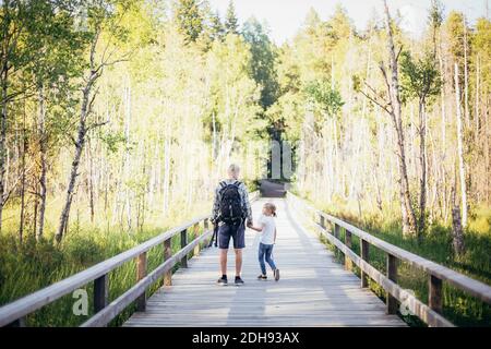 Father with backpack talking to daughter while standing on footbridge in forest Stock Photo