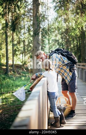 Father with backpack talking to daughter on footbridge in forest Stock Photo