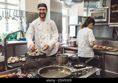 Portrait of smiling male chef cooking mushrooms in commercial kitchen Stock Photo