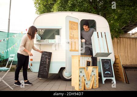 Female owner placing menu board while colleague standing in food truck on street Stock Photo