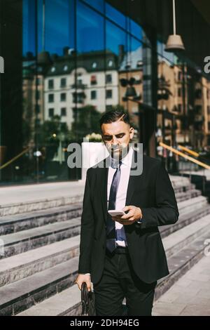 Businessman using smart phone while walking in city Stock Photo